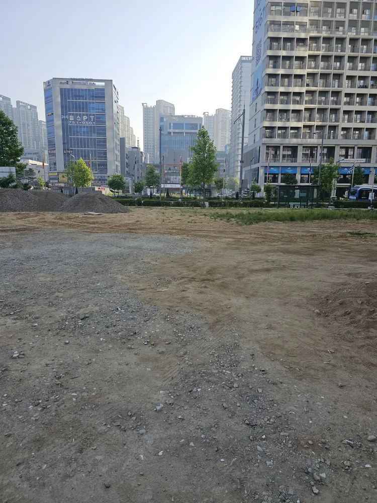골재가 고르게 펼쳐지고 롤러 자국이 남은 부지 위로 콘크리트 슬래브가 보이는 현장