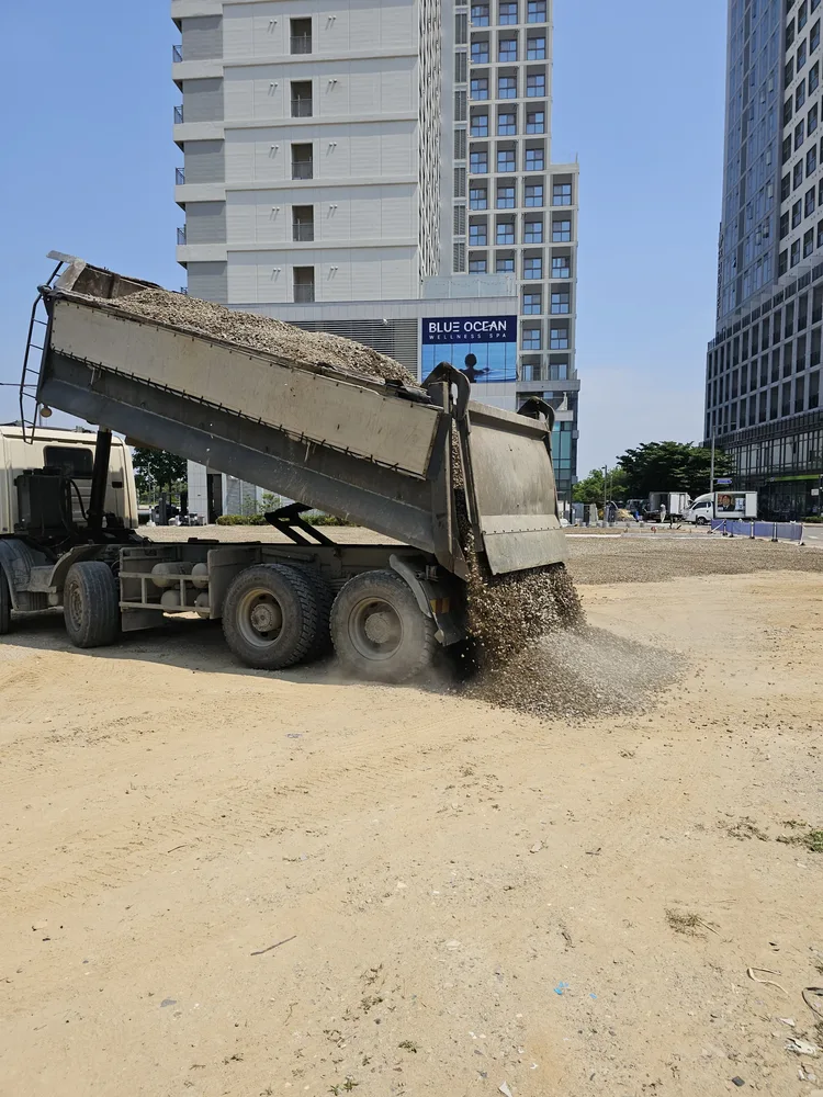 덤프트럭이 부지 한쪽에 골재와 모래를 내려놓는 주차장 골재 포설 반입 장면